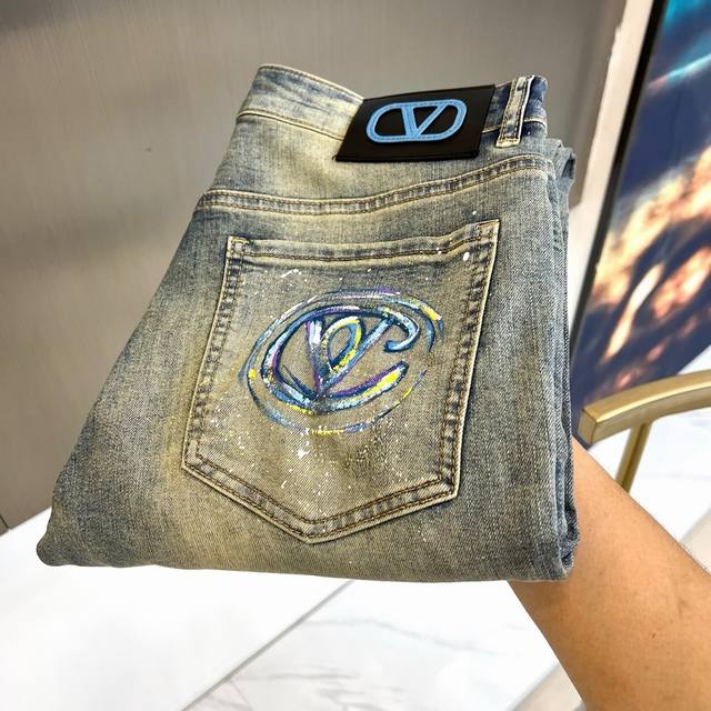 Vt华伦天奴、2026春夏新品牛仔裤，以利落剪裁勾勒随性轮廓，做旧水洗牛仔面料自带复古腔调，泼墨式细节为裤身注入街头艺术感。后袋处幻彩烫印vlogo极具视觉张力