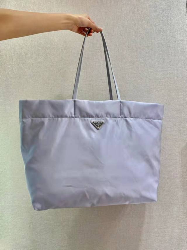 P460 新款托特包1Bg107这款中号托特包采用创新的再生尼龙面料打造，设计简约时尚。包身配有精美的Saffiano皮革提手，饰以标志性的涂珐琅三角形金属徽标