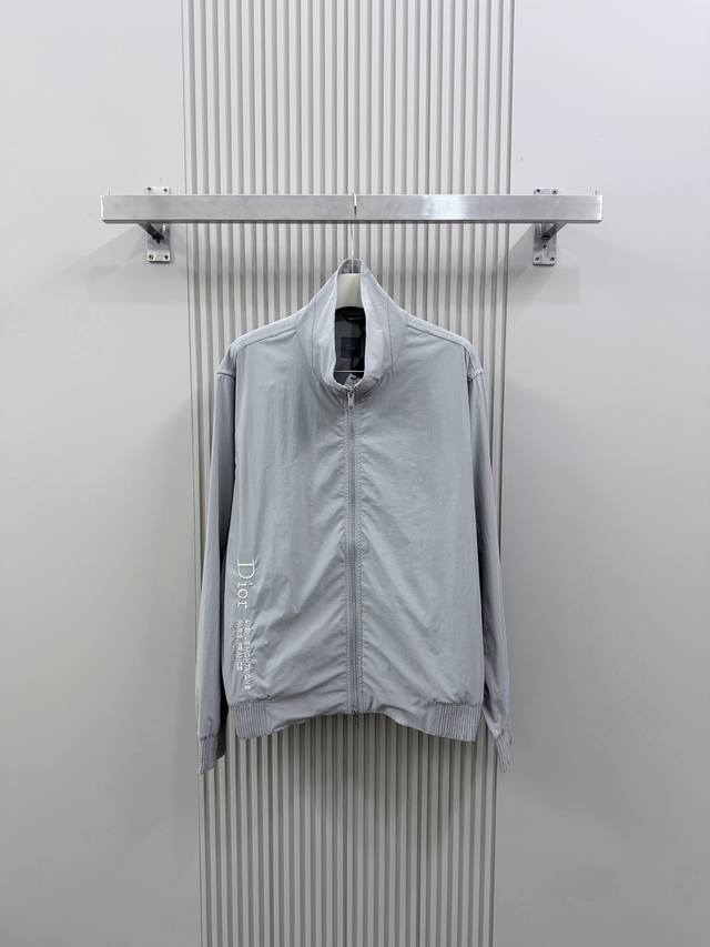 p360 迪奥 26Ss新款防风夹克为街头服饰经典单品增添了精裁风范。采用灰色科技面料精心制作，饰以 Dior Montaigne 刺绣，搭配拉链开合和连帽。可